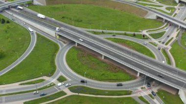 Çağdaş altyapı ve lojistiği gösteren yeşil şehir ortamında çoklu şeritler, üst geçitler, döner kavşak ve trafik ile karmaşık bir yol kavşağının yukarıdan aşağıya ve açılı insansız hava aracı görüntüsü.