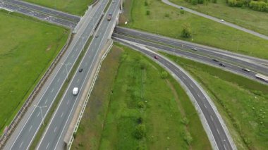 İnsansız hava aracı görüntüleri üstgeçitlerle, rampalarla ve otlakların arasında hareket eden araçlarla karmaşık bir yol değişimi gösteriyor. Modern yol mühendisliğini gösteriyor.