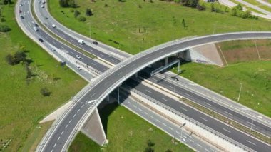 İnsansız hava aracı videosu, otlak alanlar ve hareket halindeki araçlarla çevrili çok şeritli bir yol boyunca kıvrımlı bir otoyol üstgeçidini gösteriyor. Modern yol tasarımını simgeliyor.