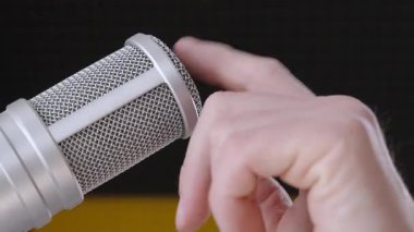 Macro, erkek elini podcast, kayıt ya da yayıncılıkta kullanılan karanlık arka planlı bir stüdyoda profesyonel bir yoğunlaştırıcı mikrofonu ayarlarken ya da hazırlarken gösterir..