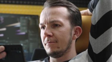 Monitörlerin önünde çalışma alanında oturan bir adamın akıllı telefonuna rastgele göz attığı görülüyor. Çevre, teknoloji ve yaşam tarzının bir ofis ortamında harmanlanmasını yansıtır.