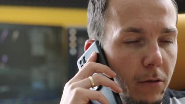 Genç bir yetişkin adam, bir telefon görüşmesi sırasında çeşitli duygusal ifadeleri gösteren, çağdaş bir çalışma alanında akıllı bir telefonla konuşurken görülüyor. Ayarlar profesyonel ya da iş iletişimi öneriyor.