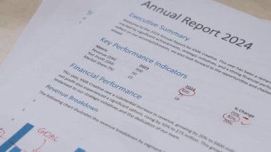 Finansal grafikler, çubuk grafikleri ve performans göstergelerini gösteren basılı iş belgelerinin ofis çalışması ve analizini temsil eden 2024 yıllık raporunda el ele tutuşması ve zımbalanması yakın plan