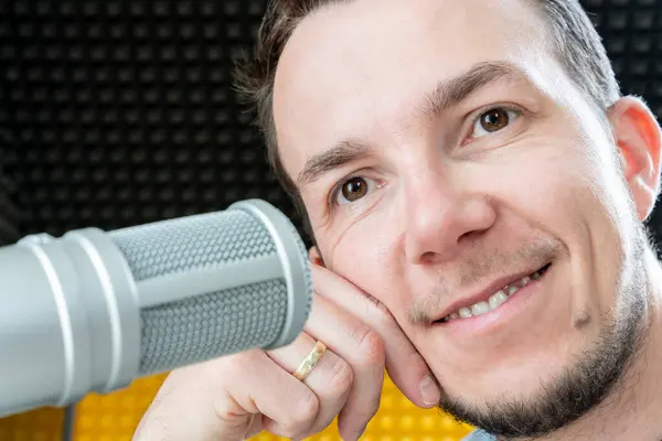 Stüdyoda profesyonel mikrofonun yanında sırıtan bir adam podcast kaydında pozitif bir ruh hali canlandırıyor.