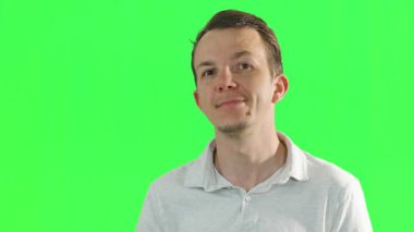 Sıradan giyinmiş genç bir adam kameraya ve yana bakıyor, yeşil ekranın önünde yüz ifadelerini onaylıyor. Medya üretiminde krom anahtar ve görsel efektler