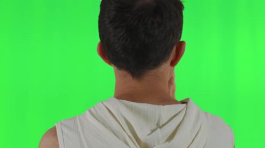 Eli başının üzerinde, sırtı yeşil arka planda kameraya dönük genç bir adam, kavramsal medya kullanımı için düşünceli ya da karışık duyguları resmediyor..