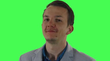 Spor ceketli genç adam, birleşik esneklik için yeşil ekranda çekilen kamerayla göz temasını sürdürürken bir dizi kurnaz gülümseme ve gevşek ifadeler sergiliyor..