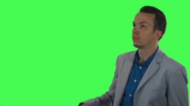 Açık gri ceketli yetişkin adam, teknoloji, yenilik veya UI / UX tasarım konuları için yeşil ekran arka planına karşı sanal bir arayüz kullanıyor gibi hareket ediyor ve işaret ediyor.