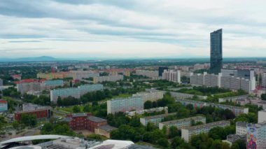 Drone görüntüleri Wroclaw kentsel yerleşim alanını gösteriyor. Arka planda ikonik Gökyüzü Kulesi ve Sleza Dağı var. Gökyüzü karamsar ve geniş bir şehir manzarası yaratıyor.