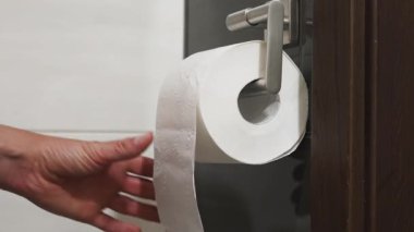 Krom gümüşü sapına asılmış tuvalet kağıdı çeken bir adamın yakın çekim videosu. Kişisel hijyen ve tuvalet ortamındaki günlük alışkanlıkları gösteriyor..