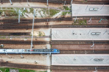 Top-down aerial view of railway platforms and single train arriving station, symmetrical layout with empty tracks and modern infrastructure