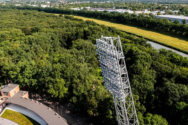Yoğun yeşil ormandan yükselen uzun projektör aydınlatma kulesi yaz havası çatısı ve nehri olan stadyum çatısı ile