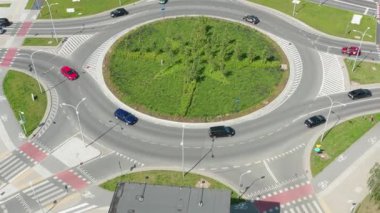 İnsansız hava aracı görüntüleri, hareket halindeki araçlarla çevrili ve parlak gün ışığında yaya geçitleri işaretlenmiş, pusula şeklinde çimenli bir merkez adayla kavşağı gösteriyor..