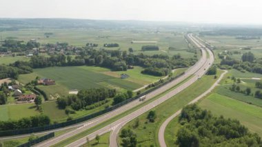İnsansız hava aracı, tarımsal tarlalardan ve hareket halindeki trafik ve açık gökyüzünün altındaki uzak yerleşim bölgelerinden geçen dolambaçlı bir otoyolu takip ediyor..