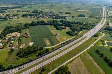 Kırsal kesimde yeşil tarlalar ve yaz boyunca dağınık köyler bulunan modern otoyolun havadan görünüşü, ulaşım planlaması