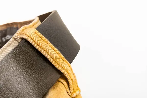 Çok az stüdyo ışığı, moda detayı ve giysi tasarımı içeren kumaş ve koyu kahverengi deri kemerli kahverengi pantolonlara yakın plan.