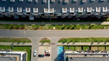 Bu insansız hava aracı görüntüsü, modern apartman binaları, peyzajlı kaldırımlar ve araçlarla çevrili bir banliyö kavşağının tepeden tırnağa görüntüsünü yakalıyor. Konut geliştirme ve altyapı düzenini gösteriyor..