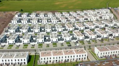 Bu eğri büğrü hava dizisi, yaz ışığı altında manikürlü çimenleri ve servis yolları olan modern beyaz kasaba evlerini inceliyor..