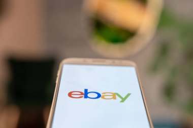 eBay logosunu ekranda gösteren akıllı telefon kişi tarafından tutuluyor, çevrimiçi pazar erişimi