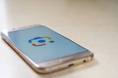 Üzerinde Google Lens logosu olan akıllı telefon parlayan odaya bakan ekranla birlikte masaya yerleştirildi