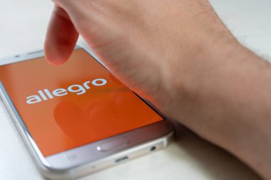 Allegro logosunu gösteren akıllı telefon ekranına dokunan kişi