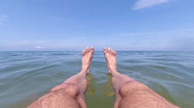 Güneşli bir günde suyun üzerinde bacakları esnemiş bir adam.