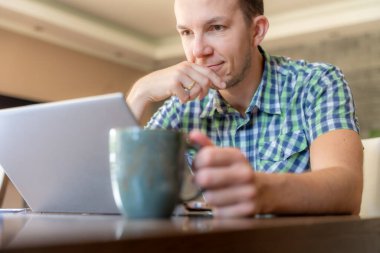 İçişleri Bakanlığı 'nın bilgisayarında çalışırken elinde kahve fincanı tutan gülümseyen adam.