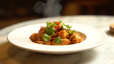 Masada beyaz bir tabakta servis edilen kişniş ve biberli leziz bir tavuk yemeğinin yakın çekimi.