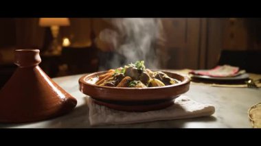 Buharı tüten bir tagine tabağı masada servis edilir, yanında tagine kapağı, tadını çıkarmaya hazır.