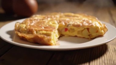 Beyaz bir tabakta İspanyol omletinin yakın plan resmi ve arka planda tahta bir masa yüzeyinde yumurtalar.