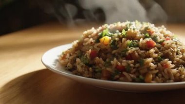 Karışık sebzeli buharda pişmiş bir tabak pirinç yumuşak, sıcak bir ışığın altında, ahşap bir yüzeye oturur.