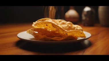 Beyaz bir tabakta yakın plan tortilla cipsi. Masadaki cipslerin üzerine baharatlar dökülüyor.