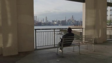 Gün batımında Brooklyn Rıhtımı 'nda bir bankta oturan tanınmayan birinin el kamerası görüntüsü. Williamsburg 'da, Brooklyn' de 4K 'da çekilmiş..