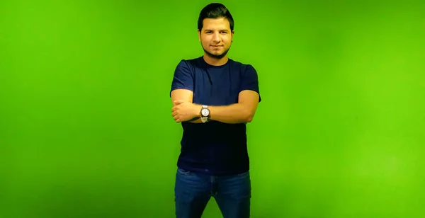 Young latin man looking forward with arms crossed on green screen