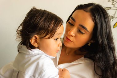 Latin bir anne kucağında bebeğiyle sevgiyle konuşur.