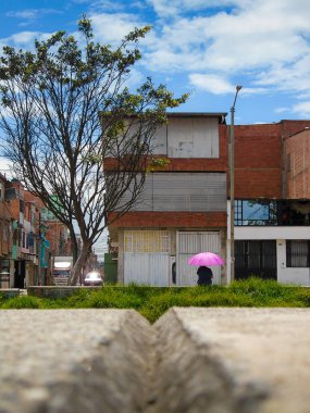 Bogota 'nın güneyinde, Bosa' da bir caddede pembe şemsiyeli bir adam oturuyor.