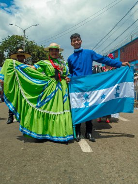 Neiva, Huila, Kolombiya - 30 Haziran 2024 - Geleneksel kostümlü Latin çiftler ve bir geçit töreninde kameraya bakan Honduras bayrağı