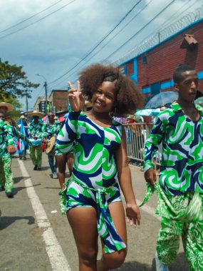 Neiva, Huila, Kolombiya - 30 Haziran 2024 - Kıvırcık saçlı, geleneksel elbiseli Latin bir kadın geçit töreninde barış ve aşk işareti yapıyor