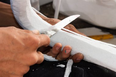 Hands of a dark-skinned Latino man cutting a piece of styrofoam with a long knife clipart