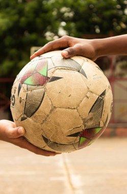 Hands of Latino children holding an old ball on a park field in Neiva - Huila - Colombia clipart