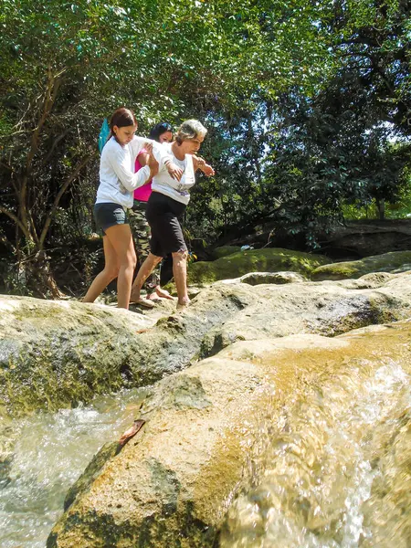 İki genç kadın, Neiva-Huila-Kolombiya 'da bir tatil gezisinde taşlardan bir nehirde yürüyen Latin bir büyükanneye yardım ediyor. Yaşlılar, seyahat ve yardım kavramı