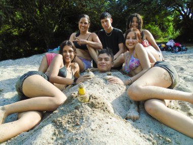 Neiva, Huila, Kolombiya 'da kırsal bir tatil sırasında arkadaşlarıyla birlikte kumsalda gömülü genç bir Kolombiyalı. Arkadaşlık, mutluluk ve yaşam tarzı kavramı