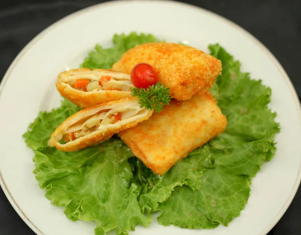 Risoles or Risol filled with ragout. Salted fried snacks in the form of envelope or triangles. The filling is consisting of vegetables, shrimps, eggs and curry. The outer shell is coated with breadcrums. Selective focus.