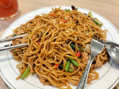 Kızarmış erişteyi sebzeli ve karidesli beyaz tabakta yakın çekim. Çubuklu baharatlı kızarmış şehriye..