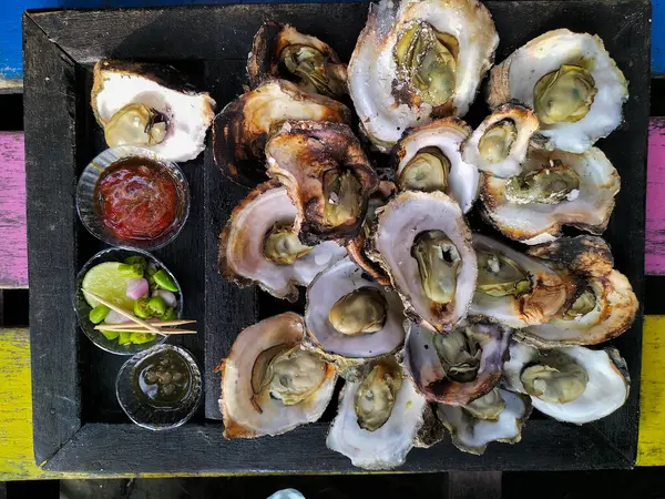 Closeup view of oysters in serving plate, medium grilled oysters with spicy seafood sauce, chilli plate, chili pieces and soy sauce. Indonesia food popular seafood menu.