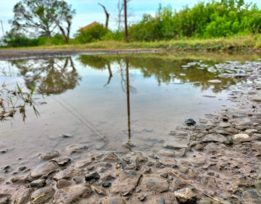 Seçici odaklanma. Endonezya tarım bölgesinde su birikintileri ve köy manzaralı bozuk bir yol. Eski bozuk yol.