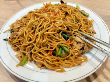 Kızarmış erişteyi sebzeli ve karidesli beyaz tabakta yakın çekim. Çubuklu baharatlı kızarmış şehriye..