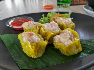 Seçici odaklanma. Shumai veya Çin Buharlı Hamur köftesi, siyah tabakla servis edilen ahlaksız derili köfte, sos ile servis edilir. Taze el yapımı gamsum..