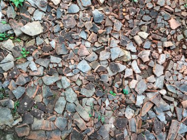 Seçici odaklanma. Kırık çatı döküntüleri, taşlar ve küçük çakıllarla birlikte yere saçılmış ve doğal pürüzlü bir dokuyla bir yüzey oluşturmuştur. Kullanılmayan kırmızı çatı kiremitleri.