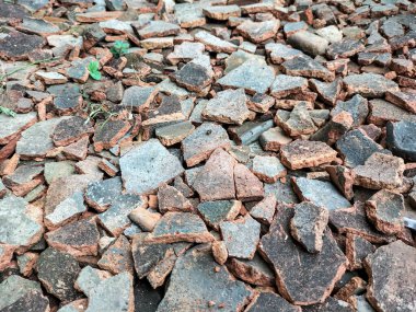 Seçici odaklanma. Kırık çatı döküntüleri, taşlar ve küçük çakıllarla birlikte yere saçılmış ve doğal pürüzlü bir dokuyla bir yüzey oluşturmuştur. Kullanılmayan kırmızı çatı kiremitleri.